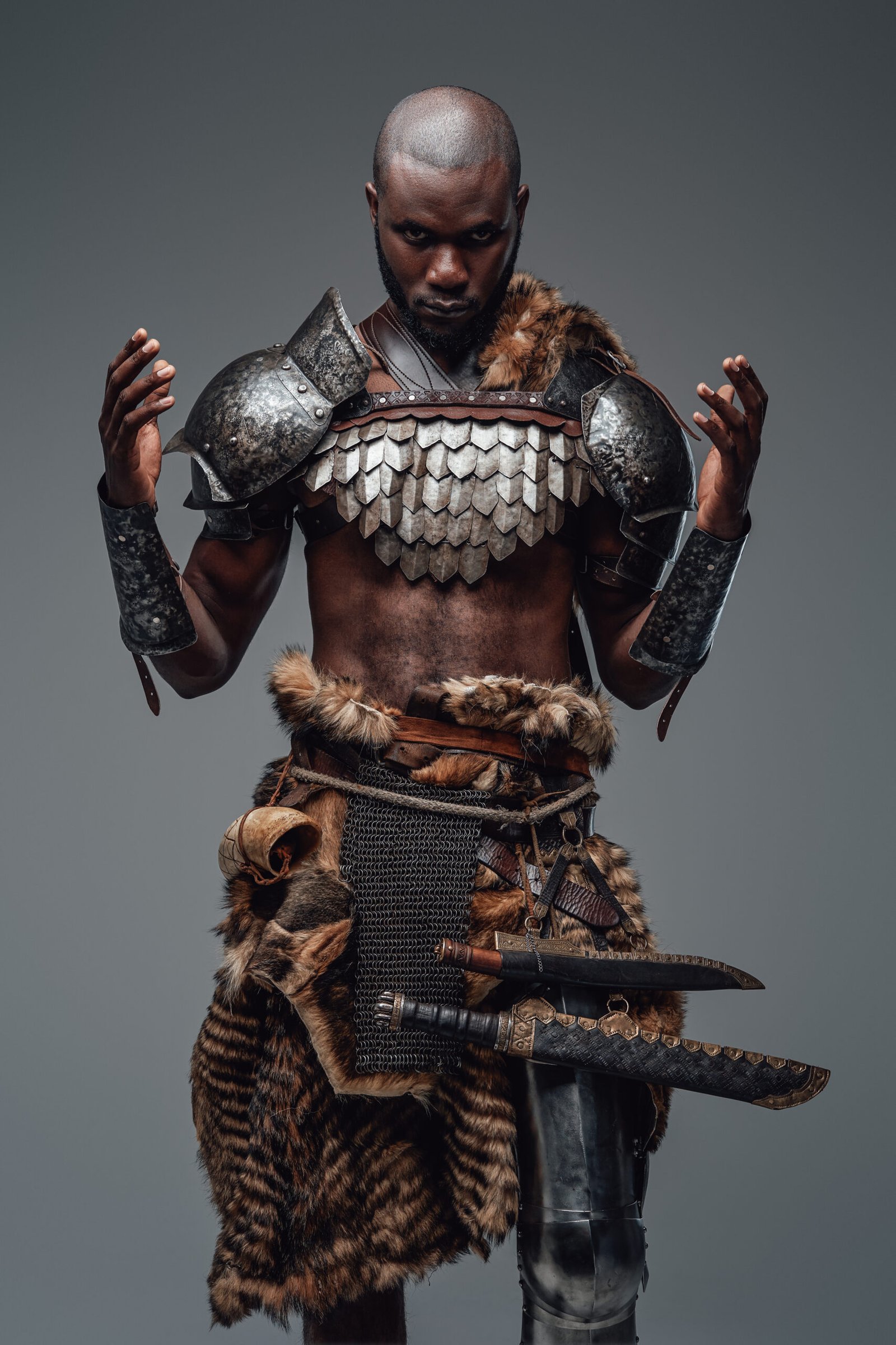 Authentic african barbarian prays with raised hands in gray background African fighter dressed in authentic clothing and armor prays to gods rising his hands. Concept of mad and spiritual warrior in gray background.